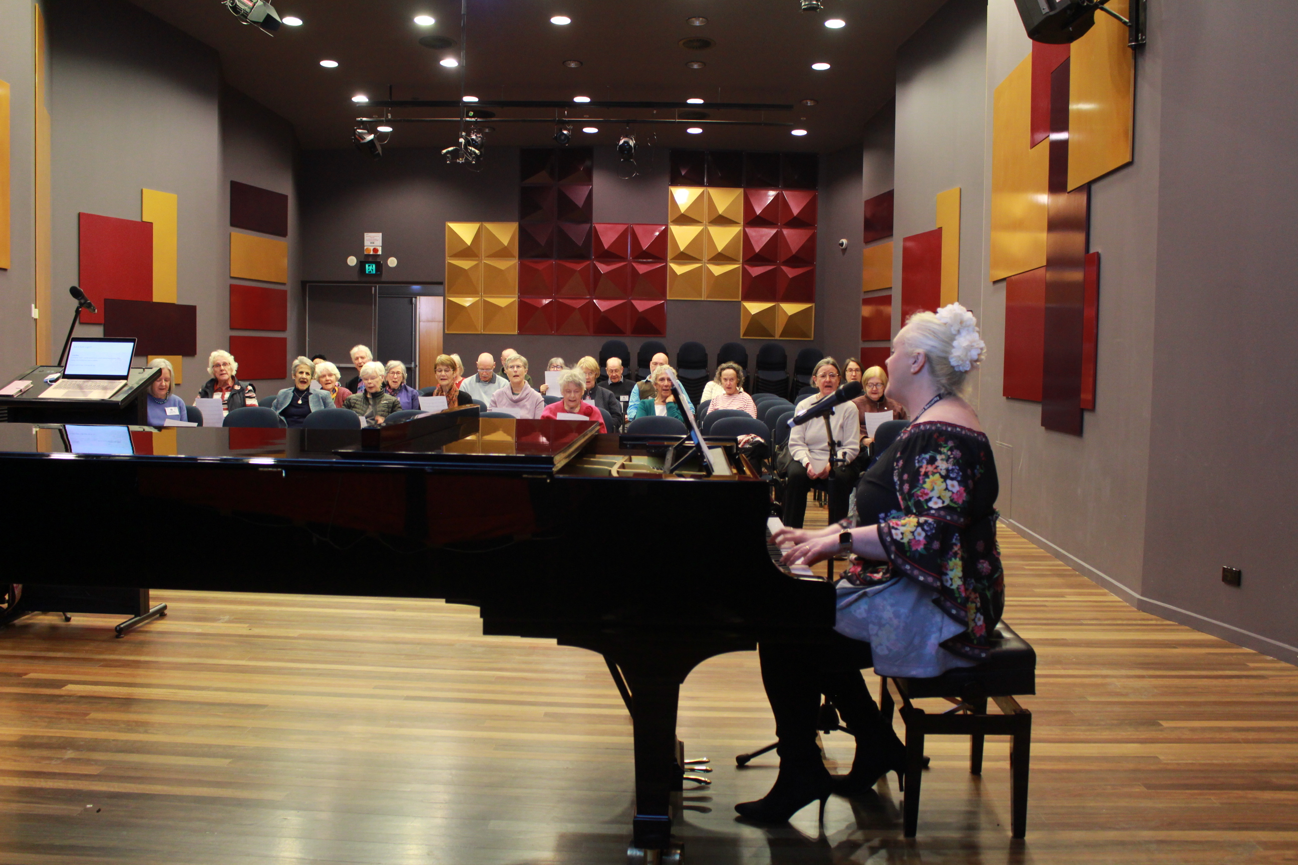 A person playing piano with an audience of senior adults singing and seated in the background